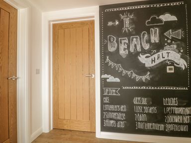 A hallway with two wooden doors and a large blackboard wall with chalk writing at The Beach Halt in Perranporth