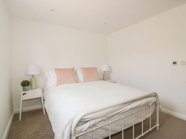 A bedroom with a bed with white linens and pink pillows two bedside tables with lamps and a small plant at The Beach Halt in Perranporth