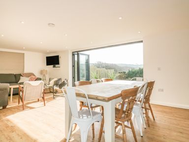 A dining area with wooden and metal chairs next to a living room with sofas and armchairs at The Beach Halt in Perranporth