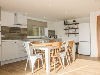 A kitchen with a wooden dining table and mixed chairs by cabinets and a refrigerator at The Beach Halt in Perranporth