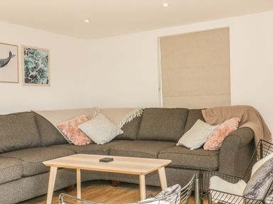 A living room with a gray corner sofa and cushions a wooden coffee table and framed pictures on the wall at The Beach Halt in Perranporth