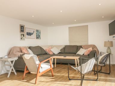 A living room with a large gray sectional sofa wooden armchair metal frame chairs coffee table and wall art at The Beach Halt in Perranporth