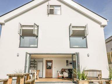A house exterior with open windows and glass doors showing a kitchen and living area at The Beach Halt in Perranporth