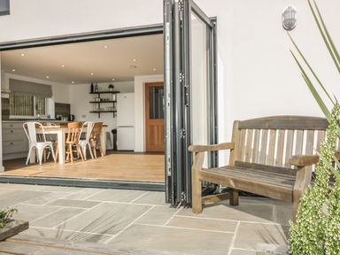A wooden bench on a stone patio outside a kitchen with dining table and chairs at The Beach Halt in Perranporth