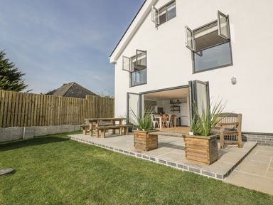 A backyard patio with wooden benches and planters next to a white house with open windows at The Beach Halt in Perranporth