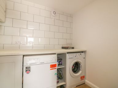 A laundry room with a washing machine and dryer under a counter at The Beach Halt in Perranporth