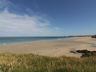 A wide sandy beach with ocean waves and grass in the foreground at The Beach Halt in Perranporth
