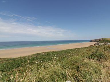 A beach with sand and ocean viewed from a grassy hillside at The Beach Halt in Perranporth
