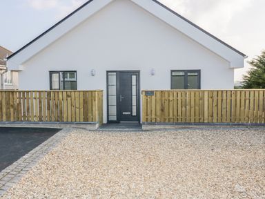 A front view of a single story house with a black door and two windows with wooden fences on both sides and gravel driveway at The Beach Halt in Perranporth