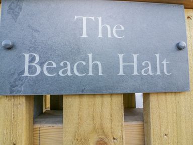 A close-up of a stone plaque with the text The Beach Halt mounted on a wooden fence