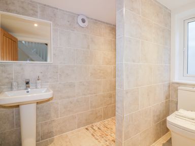 A bathroom with a pedestal sink mirror and toilet next to a walk in shower at The Beach Halt in Perranporth