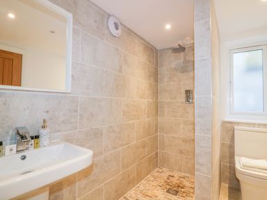 A bathroom with a wall-mounted sink a walk-in shower with a rain showerhead and a toilet with folded towels on the lid at The Beach Halt in Perranporth