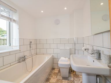 A bathroom with a bathtub toilet and sink with tiled walls and patterned floor at The Beach Halt in Perranporth