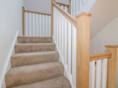 A carpeted staircase with wooden handrails and white spindles at The Beach Halt in Perranporth