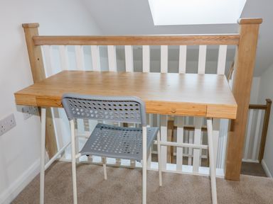A wooden desk with a gray chair on a carpeted floor next to a wooden and white railing at The Beach Halt in Perranporth