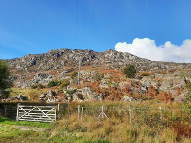 A rocky hillside with grass and a wooden gate in the foreground at Bryn Alun in Tanygrisiau near Blaenau Ffestiniog