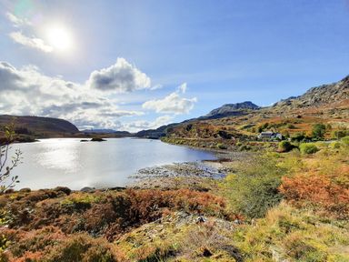 A lake surrounded by hills and vegetation with a house near the shore at Bryn Alun in Tanygrisiau near Blaenau Ffestiniog
