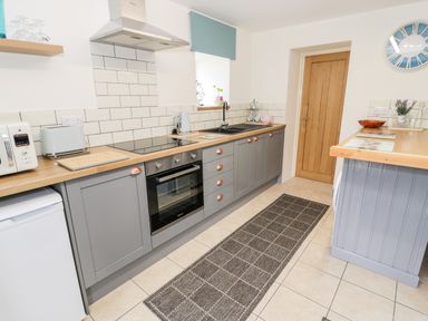 A kitchen with gray cabinets wooden countertops a stove sink microwave toaster and a rug on the tiled floor at Bryn Alun in Tanygrisiau near Blaenau Ffestiniog