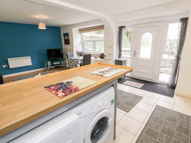 A kitchen area with a washing machine and wooden countertop overlooking a living room with a dining table and television at Bryn Alun in Tanygrisiau near Blaenau Ffestiniog
