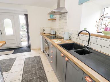 A kitchen with gray cabinets black sink oven and tiled floor at Bryn Alun in Tanygrisiau near Blaenau Ffestiniog