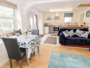 A kitchen and dining area with a small table and two chairs a sofa with cushions and a kitchen unit with oven fridge and microwave at Bryn Alun in Tanygrisiau near Blaenau Ffestiniog