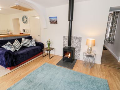 A living room with a blue sofa, wood burning stove, side tables with flowers and a lamp at Bryn Alun in Tanygrisiau near Blaenau Ffestiniog