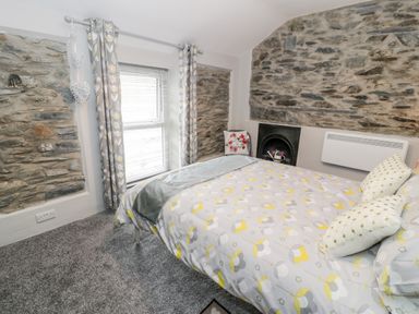 A bedroom with a bed covered in patterned bedding grey curtains on a window and exposed stone walls at Bryn Alun in Tanygrisiau near Blaenau Ffestiniog