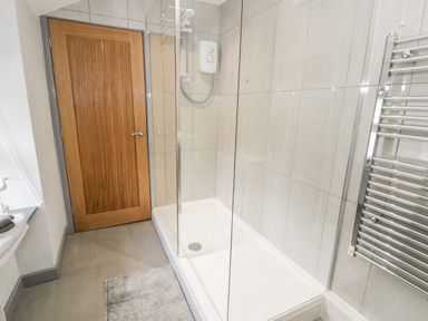 A shower area with glass partition a wooden door a towel radiator and a bath mat at Bryn Alun in Tanygrisiau near Blaenau Ffestiniog