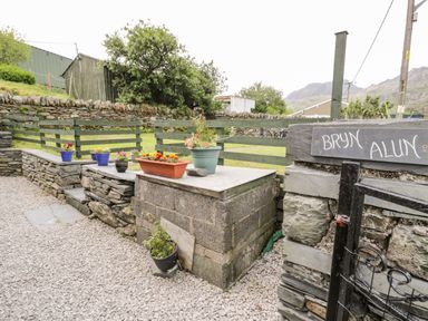An outdoor stone patio area with flower pots on a stone ledge and a green wooden fence at Bryn Alun in Tanygrisiau near Blaenau Ffestiniog