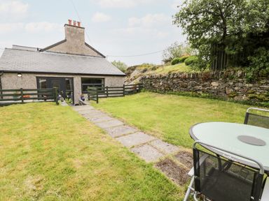 A garden with a stone path leading to a house with fenced area and outdoor table and chairs at Bryn Alun in Tanygrisiau near Blaenau Ffestiniog