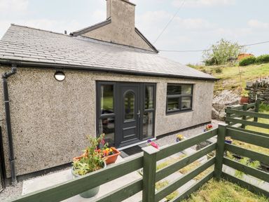 The exterior of a single-story house with a grey door and windows a green wooden fence and potted plants at Bryn Alun in Tanygrisiau near Blaenau Ffestiniog