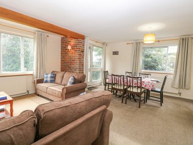 A living room with brown sofas and a dining table with six chairs and a floral tablecloth at Swan Dyke Cottage Horning near Wroxham