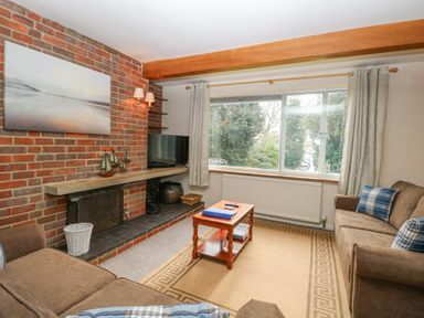 A living room with two brown sofas a wooden coffee table and a brick fireplace at Swan Dyke Cottage Horning near Wroxham