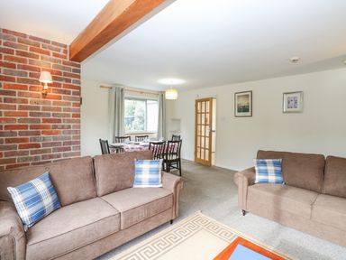 A living room with two brown sofas and plaid cushions and a dining table with chairs near a window at Swan Dyke Cottage in Horning near Wroxham
