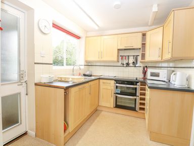 A kitchen with wooden cabinets a double oven a microwave a kettle and a window at Swan Dyke Cottage in Horning near Wroxham