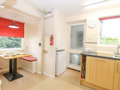 A kitchen with a table set with cups and a teapot red window blinds and a door next to a small fridge at Swan Dyke Cottage in Horning near Wroxham