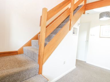 A carpeted staircase with wooden banister next to a white wall and door at Swan Dyke Cottage in Horning near Wroxham