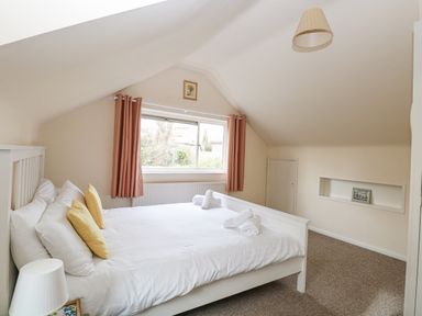 A bedroom with a white bed, pillows, rolled towels, window with curtains, a lamp, and a picture frame at Swan Dyke Cottage in Horning near Wroxham