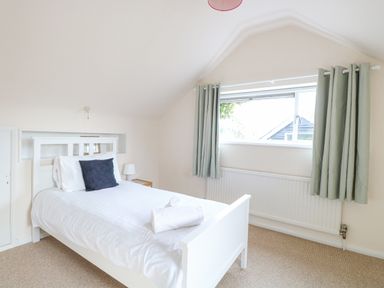 A bedroom with a white bed with pillows and towel near a window with green curtains at Swan Dyke Cottage in Horning near Wroxham