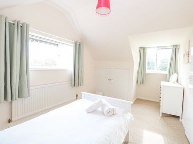 A bedroom with a bed and rolled towels next to windows with light green curtains at Swan Dyke Cottage in Horning near Wroxham
