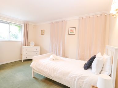 A bedroom with a single bed with white bedding and pillows a white dresser under a window with curtains and wall art at Swan Dyke Cottage in Horning near Wroxham