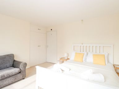 A bedroom with a white bed with yellow pillows a gray armchair and white closets at Swan Dyke Cottage in Horning near Wroxham