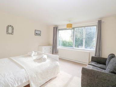 A bedroom with a bed with rolled towels a gray sofa a white dresser and a large window at Swan Dyke Cottage in Horning near Wroxham