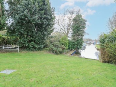A grassy garden with trees and a view of a river with boats at Swan Dyke Cottage in Horning near Wroxham