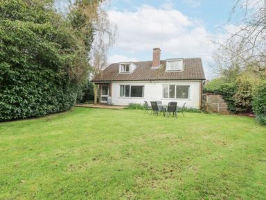 A garden with a lawn and outdoor table and chairs in front of a white house with a tiled roof at Swan Dyke Cottage in Horning near Wroxham