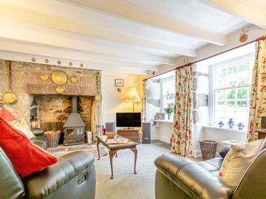 A living room with leather chairs a stone fireplace with a stove floral curtains and a television at Westside Cottage in Cardinham near Bodmin