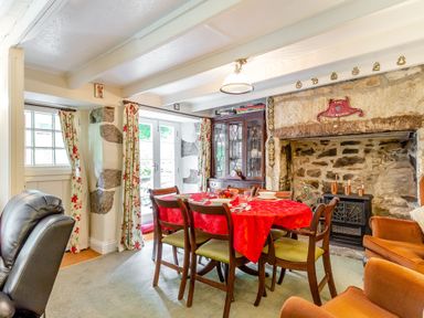 A dining room with a red tablecloth on the table and a large stone fireplace at Westside Cottage in Cardinham near Bodmin