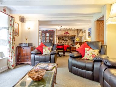 A living room with leather armchairs and a read table near a stone fireplace at Westside Cottage in Cardinham near Bodmin