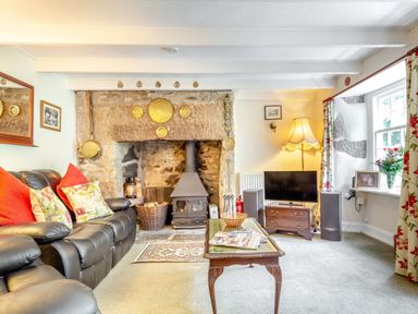 A living room with a leather sofa wooden coffee table stone fireplace and television at Westside Cottage in Cardinham near Bodmin