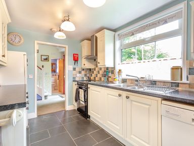 A kitchen with white cabinets a double sink a black stove and a large window at Westside Cottage in Cardinham near Bodmin